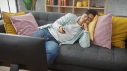 A many lazily lays on the couch. Learn more about 10 telltale marijuana addiction symptoms here.