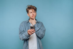 A man thinking as he looks at his phone. Learn more about the legalization of marijuana and if it makes marijuana safe, here.