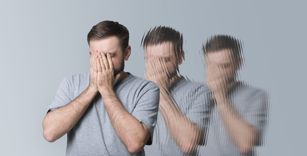 A man grips his face as he hallucinates. Learn more about the effects and risks of hallucinogens here.