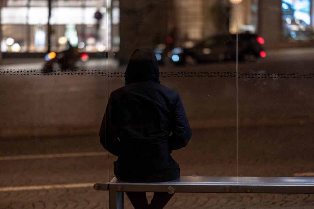 A man sitting on a bus stop bench in the city. Learn more about heroin street names and slang for heroin use here.