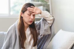 A woman grips her forehead, feeling ill. Learn more about Vicodin side effects and addiction signs here.